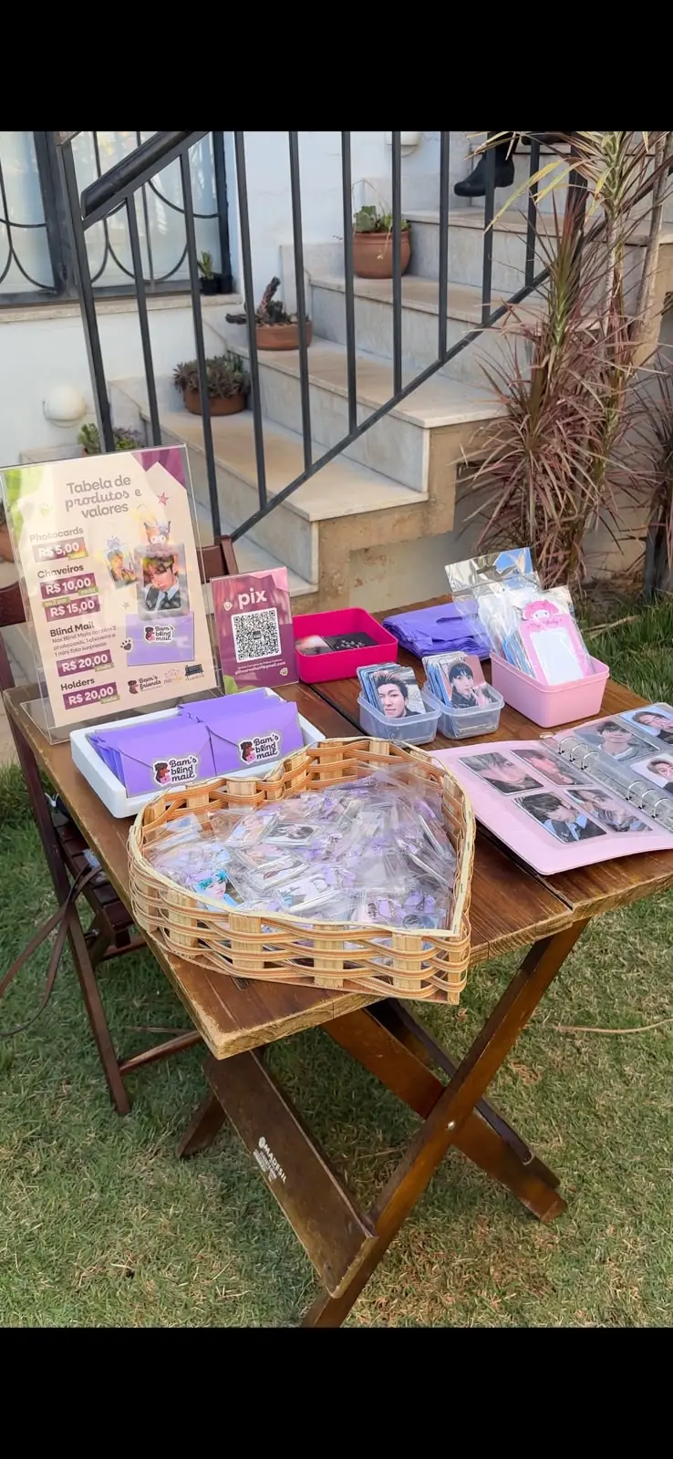 Mesa com produtos do Bam's Friends à venda no evento: photocards, chaveiros e QR code do PIX.